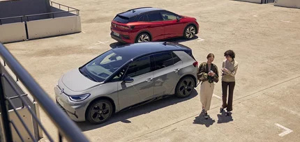 Zwei parkende VW ID Modelle in der Seitenansicht auf einem Parkplatz mit zwei Personen davor, die sich unterhalten