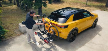 Mann befestigt ein Fahrrad auf einem Hecktr&auml;ger an einem gelben Audi SUV.